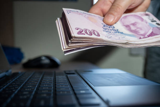 Hand holding a large number of 200 Turkish liras Hands holding a large number of 200 Turkish liras. Taken from the top angle. Laptop on the desktop in the background. para birimi stock pictures, royalty-free photos & images