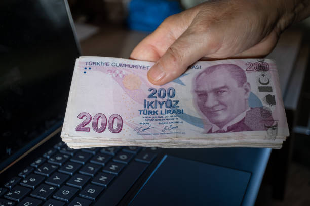 Hand holding a large number of 200 Turkish liras Hands holding a large number of 200 Turkish liras. Taken from the top angle. Laptop on the desktop in the background. para birimi stock pictures, royalty-free photos & images