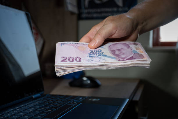 Hand holding a large number of 200 Turkish liras Hands holding a large number of 200 Turkish liras. Taken from the top angle. Laptop on the desktop in the background. para birimi stock pictures, royalty-free photos & images