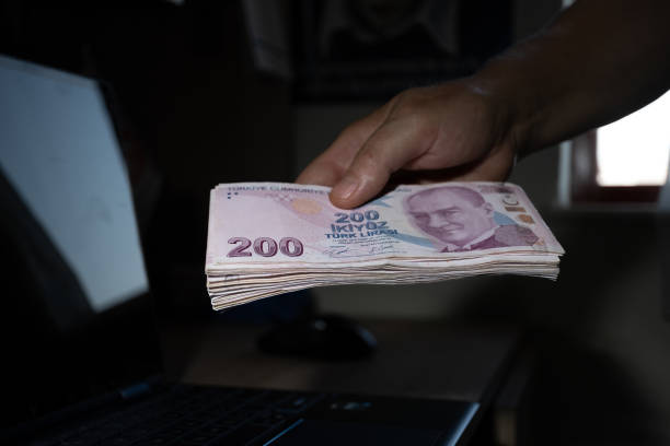 Hand holding a large number of 200 Turkish liras Hands holding a large number of 200 Turkish liras. Taken from the top angle. Laptop on the desktop in the background. para birimi stock pictures, royalty-free photos & images