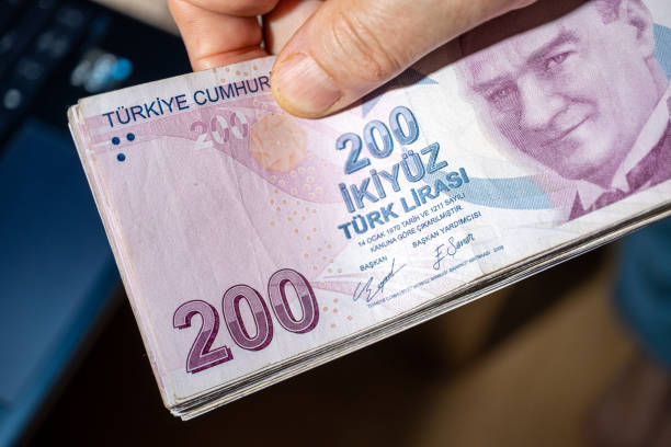 Hand holding a large number of 200 Turkish liras Hands holding a large number of 200 Turkish liras. Taken from the top angle. Laptop on the desktop in the background. para birimi stock pictures, royalty-free photos & images