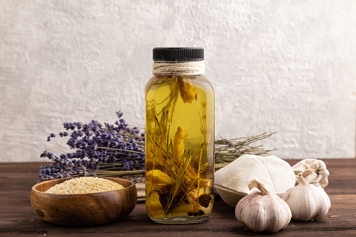 Sunflower oil in a glass jar with various herbs and spices, lavender, sesame, rosemary on a brown wooden background. Side view, copy space.