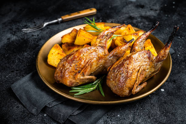 istock Delicious roasted quails with herbs in a plate with fried potato. Black background. Top view 1499722209