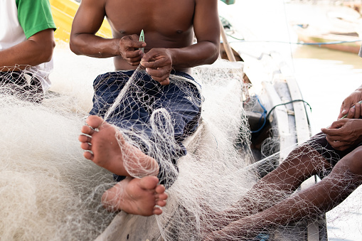 The man is repairing a fishing net on a boat in a village, Indonesia