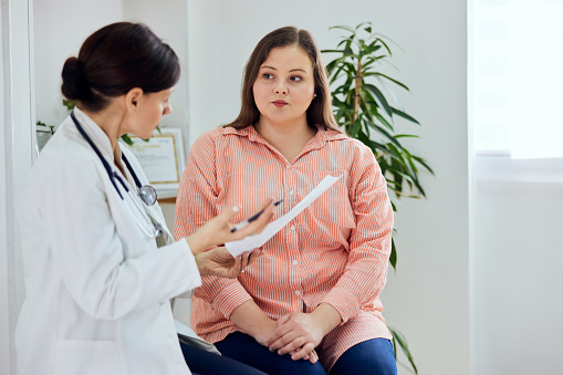 An adult pretty plus size woman sitting and talking with a female doctor about her general health condition.