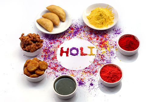 Scattered Gulal (Colored Powder) on white background and some of colored powder in the bowl and some of food in the bowl on Holi festival.