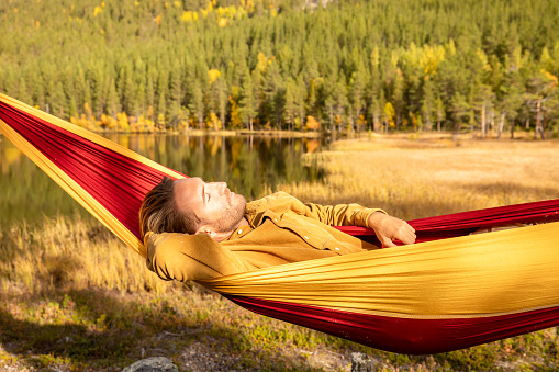 Man camping in nature relaxes on an hammock by a spectacular lake