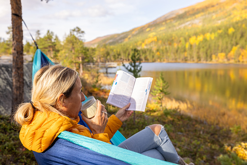 Female camping in nature relaxes on an hammock by spectacular lake in autumn, beautiful colours. Solitude and relaxation concept