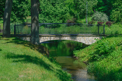 A stone bridge with a metal railing over a river among greenery, cloeup