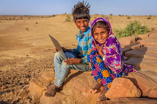 Group of happy Gypsy Indian children using laptop in desert village, Thar Desert, Rajasthan, India.