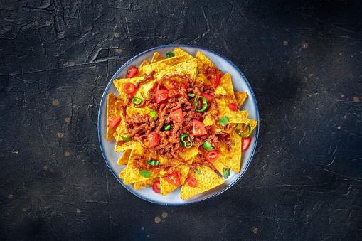 Nachos, Mexican food, tortilla chips with beef and fresh vegetables, overhead flat lay shot on a black slate background