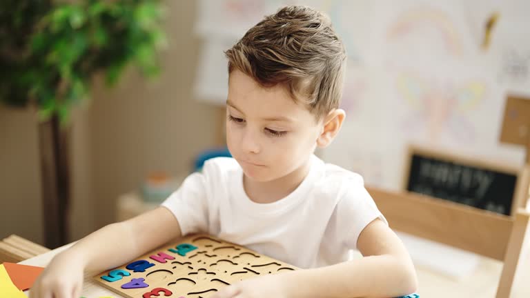 Adorable caucasian boy playing with maths puzzle game sitting on table at kindergarten