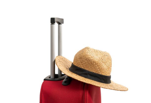 For travel and vacations purposes, a simple modern suitcase in red color is nicely isolated on a pure white background with a straw hat.