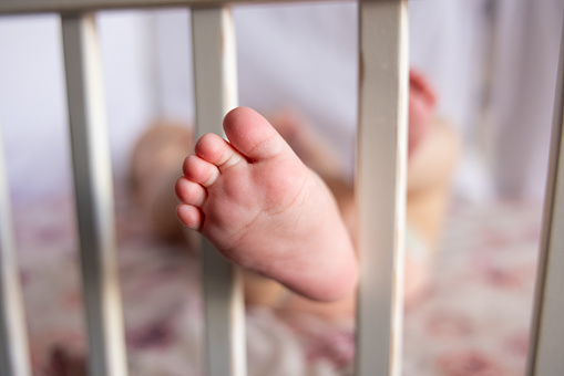 Close-up of the unrecognizable baby feet, pass through baby crib