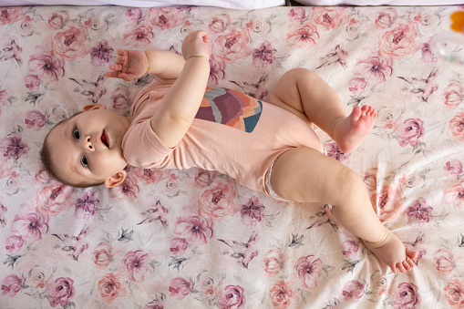 High angle view of adorable Caucasian baby girl, trying to roll on the side, while lying in the crib