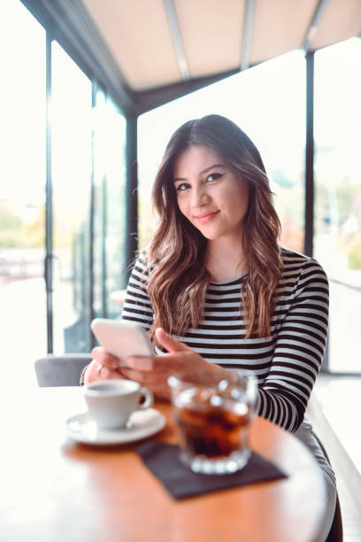 istock Cute Female Smiling Seductively While Enjoying Coffee And Drinks While Checking Social Media On Smartphone 1499752096