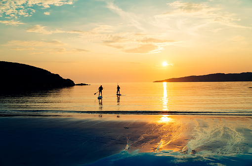 Young couple surfboarding at Achmelvich Bay, on the West Coast of Scotland, at sunset, after everyone else has gone.