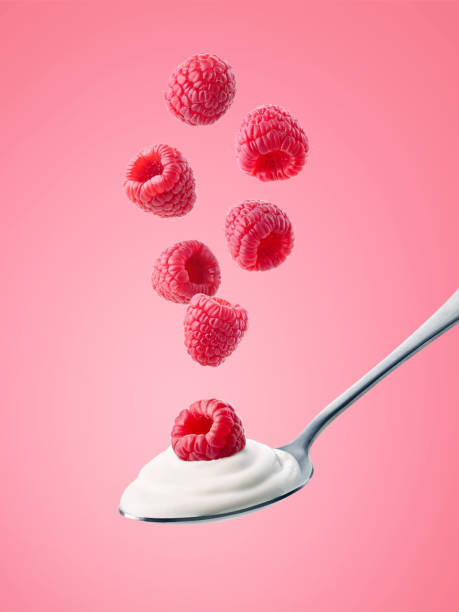 löffel frischer griechischer joghurt und fallende himbeeren auf rosa hintergrund - falling fruit berry fruit raspberry stock-fotos und bilder