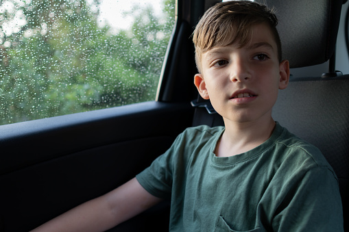 Sad boy in a car looks out the closed window while it's raining outside.
