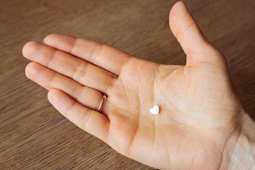 White pill on open palm hand. Heart shape pill in hand. Medical treatment. Painkiller from unhappy love. Therapy prescription. Health care concept. Hospital meds. Health and illness.