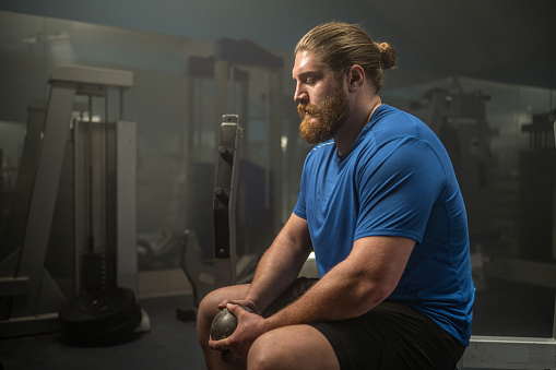 Athlete man holding shot put ball while sitting on bench in gym.