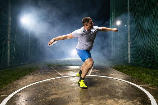 Athlete man throwing discus on track during practice at night.