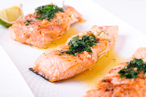 Fried trout steaks served with butter, herbs and garlic on white plate. Hot keto meal