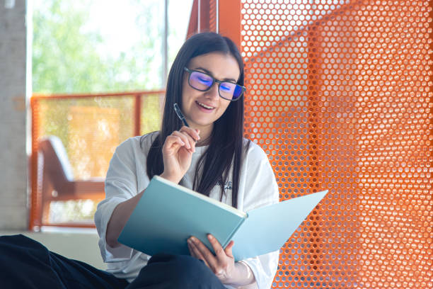 istock Young woman with glasses and notebook in modern interior, study concept. 1499766183