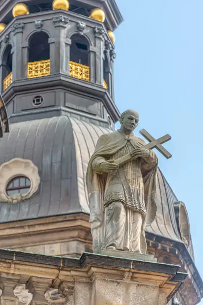 Photo of Old roof statute of priest or monk holding a big cross at Dome base of the Cathedral of Holy Trinity, historical center of Dresden, Germany.