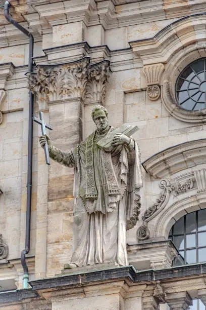 Photo of Old roof statute of priest or monk holding a big cross at Dome base of the Cathedral of Holy Trinity, historical center of Dresden, Germany.