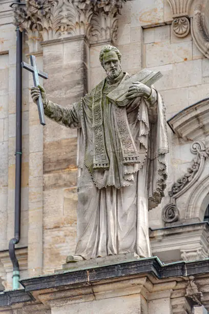 Photo of Old roof statute of priest or monk holding a big cross at Dome base of the Cathedral of Holy Trinity, historical center of Dresden, Germany.