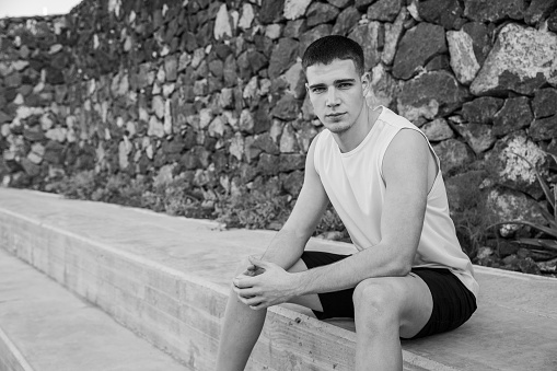 A teenage boy is sitting at the edge of a basketball court, black and white photo