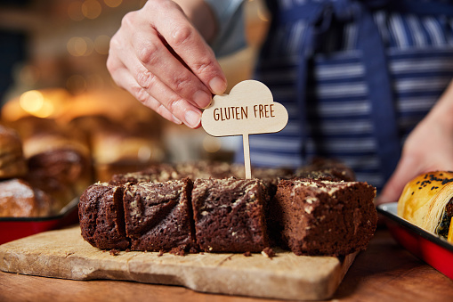Sales Assistant In Bakery Putting Gluten Free Label Into Freshly Baked Brownies