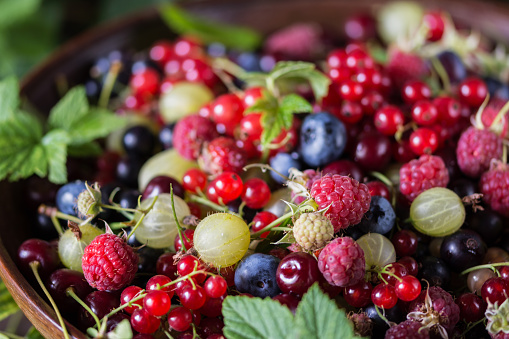 Freshly gathered juicy colorful berries inside on wooden table, mix of various berries in brown plate in brown plate, berries close up