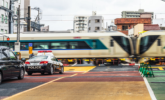 Tokyo, Japan - A police car and other traffic waiting at a level crossing in Sumida, as a passenger train crosses the street.