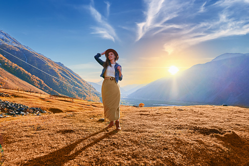 Happy smiling cute hipster woman traveler wanderer wearing hat and backpack walking alone in mountain valley, enjoying freedom and calm inspired travelling
