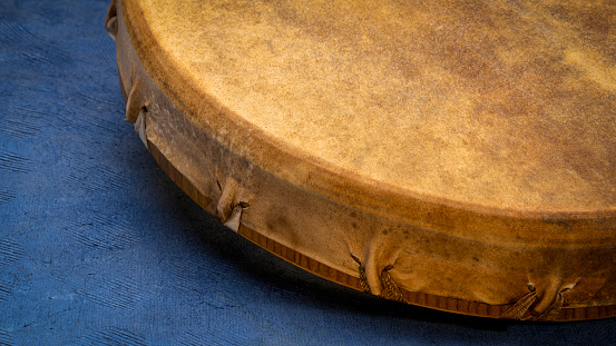 detail of handmade, native American style, shaman frame drum against textured blue paper