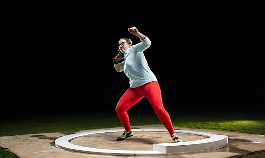 Female athlete throwing shot put ball on track during practice at night in athlete arena. Sport and healthy lifestyle concept.