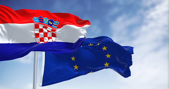 The flags of Croatia and the European Union fluttering together on a clear day. Croatia has been a member of the eurozone since January 1, 2023. 3D illustration render. Fluttering fabric