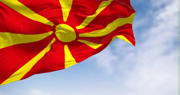 The national flag of North Macedonia that waving in the wind on a clear day. Stylized yellow sun with eight rays extending to the edges of a red field. 3d illustration render. Fluttering fabric.