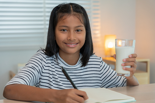 children women drink milk to nourish the body and nourish the brain. asian young little girl learn at home. girl happy drink milk and read a book for exam, Homeschool. education, vitamins, development