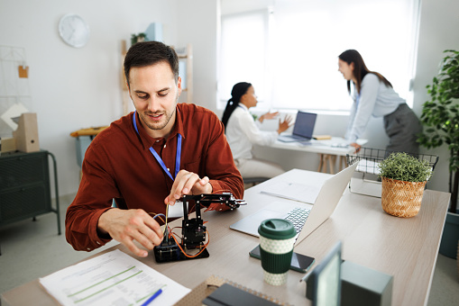 Young smiling man working on robotic arm at the office