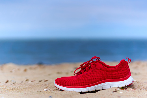 Red ladies sneaker shoes on empty sandy beach. Footwear for sport and leisure on the sea. Close up.