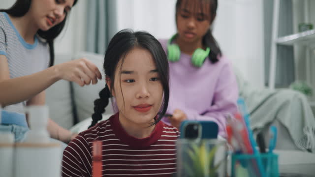 Young asian woman applies a braid for their elder sister. Two girl braids another girl's hair.