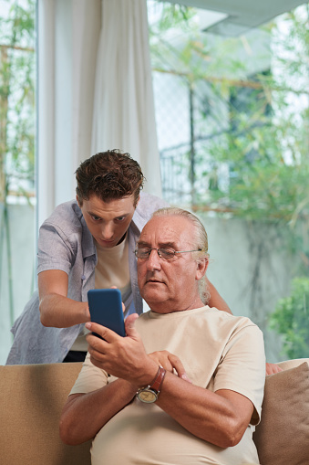 Senior man asking grandson to help him with mobile application on smartphone