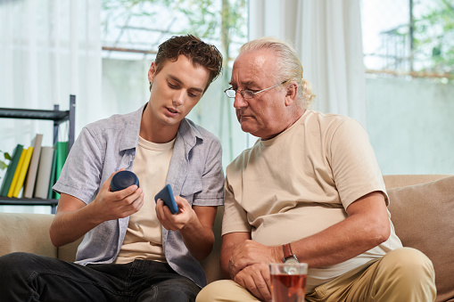 Young man explaining grandfather how to connect smartphone with speaker