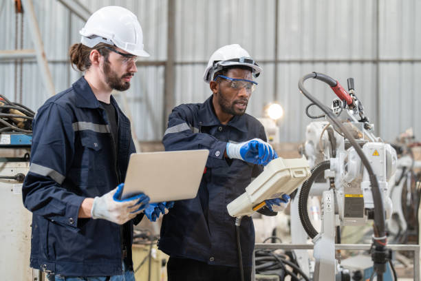 istock Male engineers wearing vest with helmet safety using labtop and remote controller control inspection robot arm welding machine in factory. Team of technician automation robot system. 1499800253