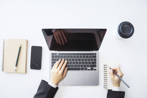 istock Detailed view of a woman's hand jotting down notes in a notepad on a modern laptop, with a blurred background 1499801405