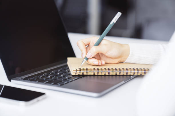 istock A woman's hand inscribing in a notepad on a modern laptop, captured closely, with a vague background 1499801447