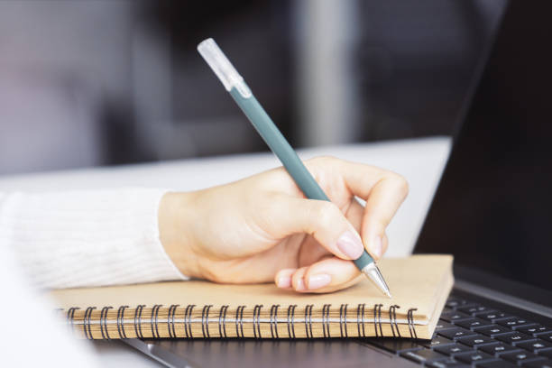 istock A woman's hand inscribing in a notepad on a modern laptop, captured closely, with a vague background 1499801454